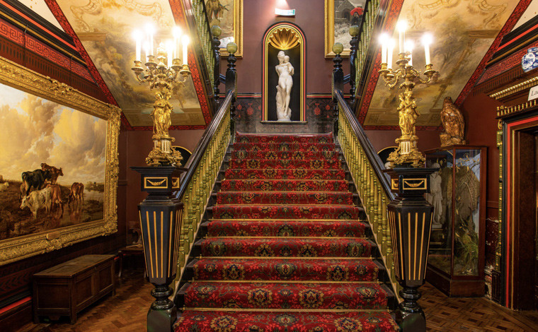 Interior of Russell Cotes art gallery & museum showing fancy staircase, paintings, ornaments and statues.